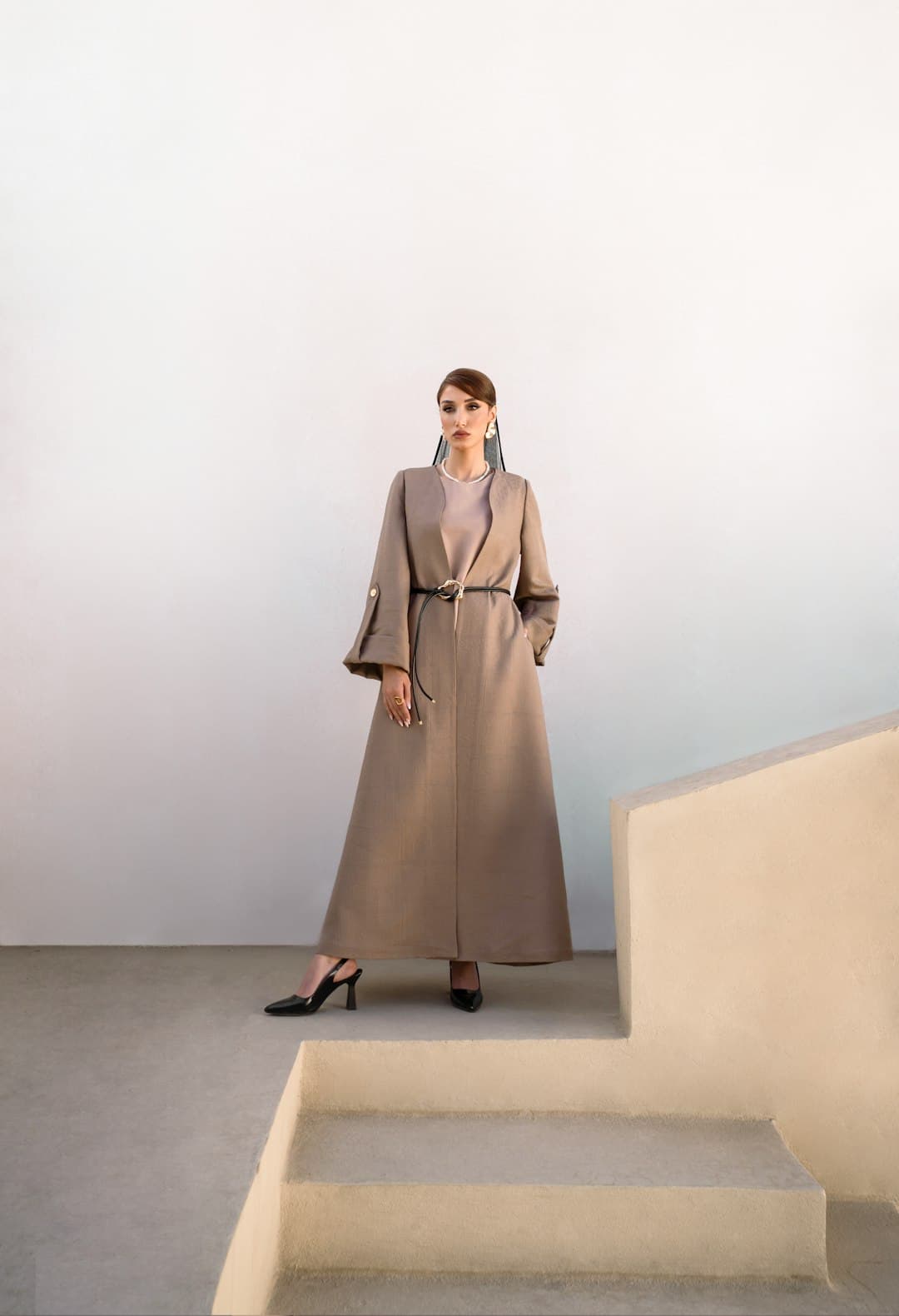 A model in a flowing abaya standing on stone steps